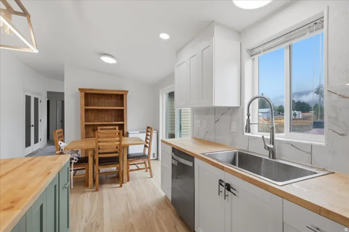 Kitchen featuring wood-finish countertops, white cabinetry, a stainless steel sink with a gooseneck faucet, a white tile backsplash, and wood-finish flooring