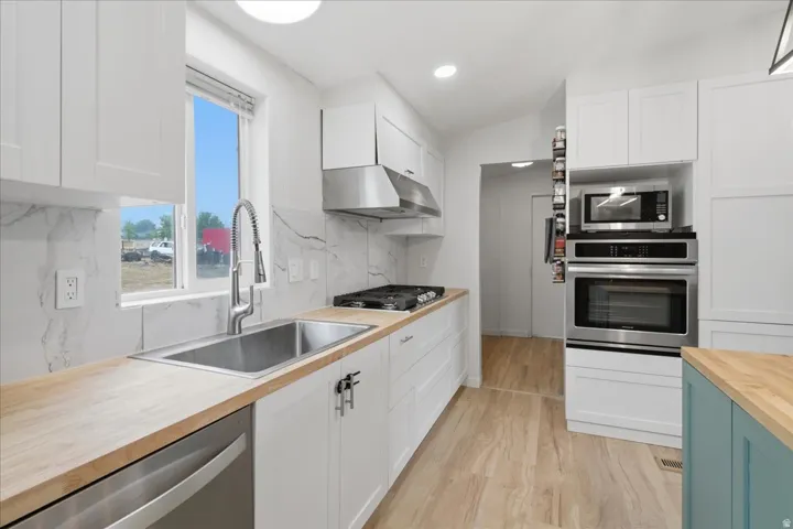 White shaker cabinetry, butcher block countertops, stainless steel appliances, marble-look tile backsplash, and light wood-finish flooring