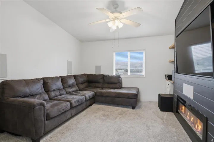 Vaulted ceiling with a ceiling fan, recessed window, built-in electric fireplace, and mounted entertainment unit