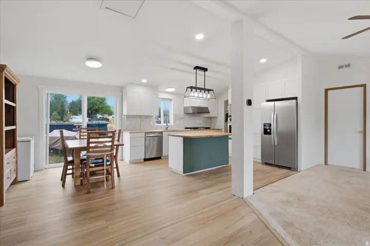 Open-concept living space with wood-finish flooring, white cabinetry, a kitchen island with a wood countertop, stainless steel appliances, and a sliding glass door