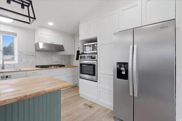 Kitchen featuring wood-finish flooring, white cabinetry, integrated stainless steel appliances, and a marble-patterned backsplash