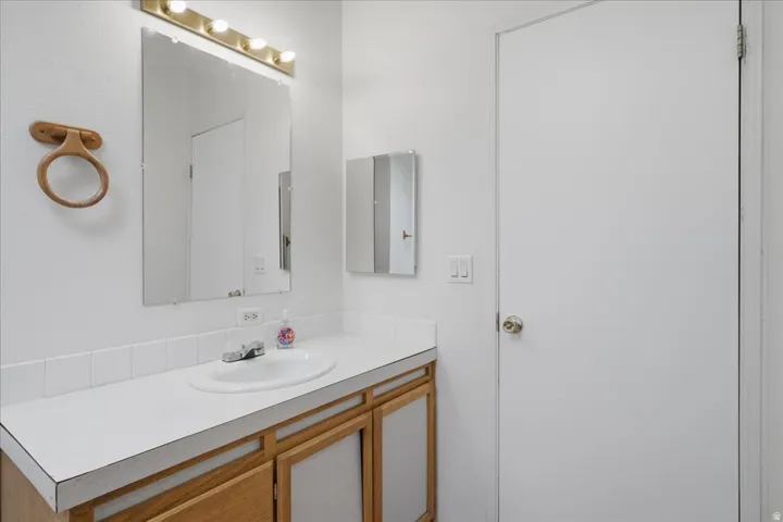 White vanity countertop with an integrated sink, framed by a large mirror and brass-finish lighting