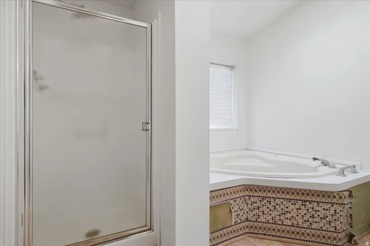Frosted glass shower enclosure, corner soaking tub, integrated tub deck with tile mosaic surround, and window with horizontal blinds