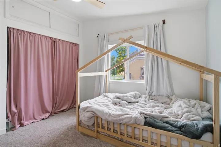 Carpeted room featuring a window with natural light, white walls, and a recessed wardrobe opening with curtain