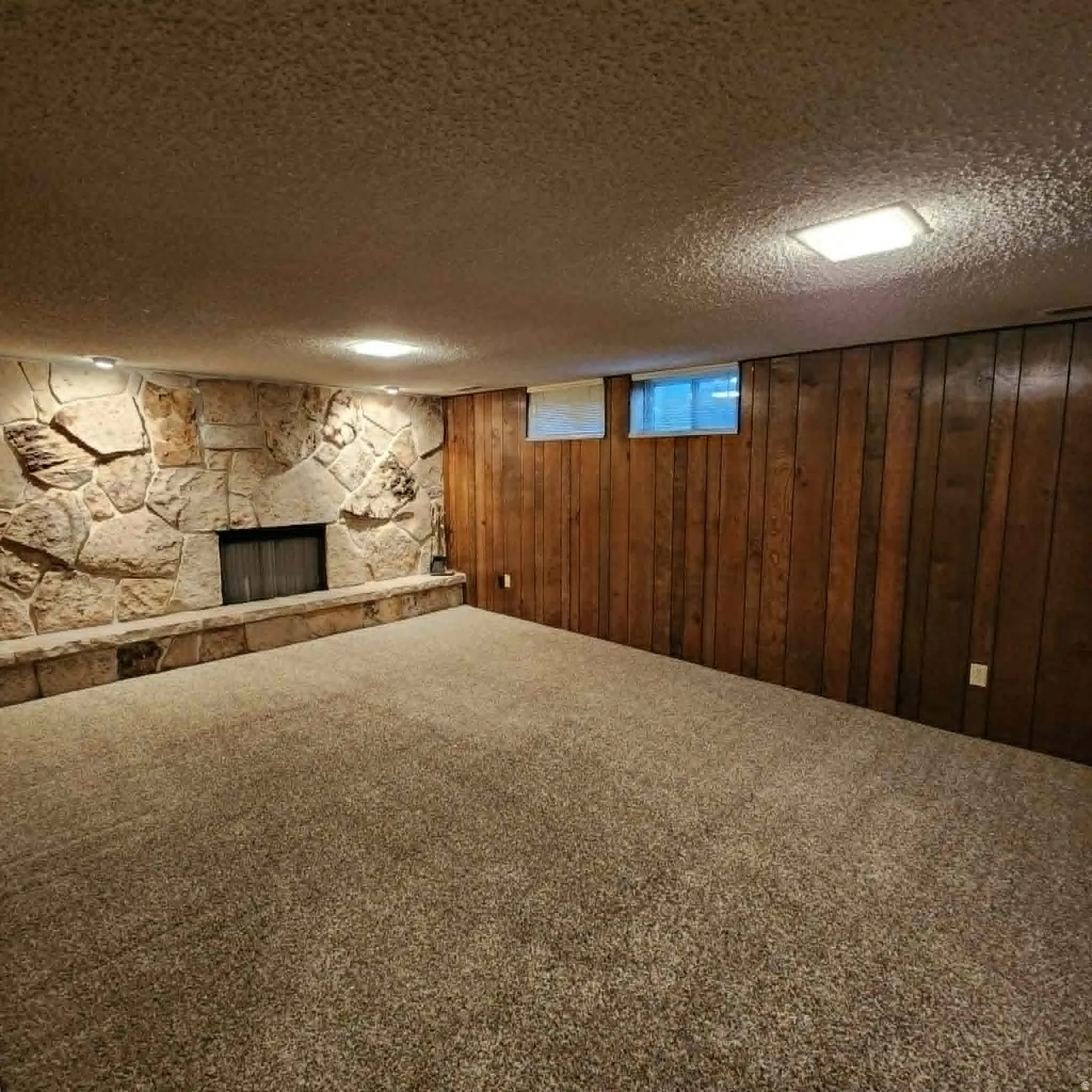 Stone-clad fireplace with hearth, wood paneling, carpeted flooring, and recessed lighting