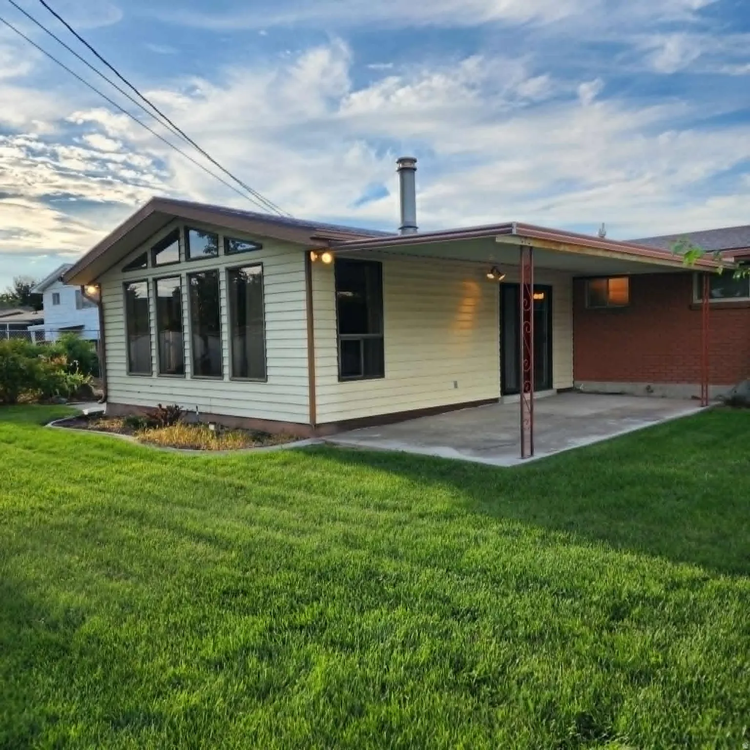 Expansive lawn area with a concrete patio, covered outdoor living space, and a distinct window wall