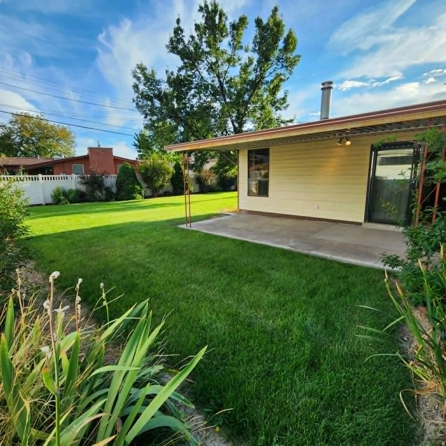 Expansive backyard featuring a manicured lawn, concrete patio, and covered outdoor area