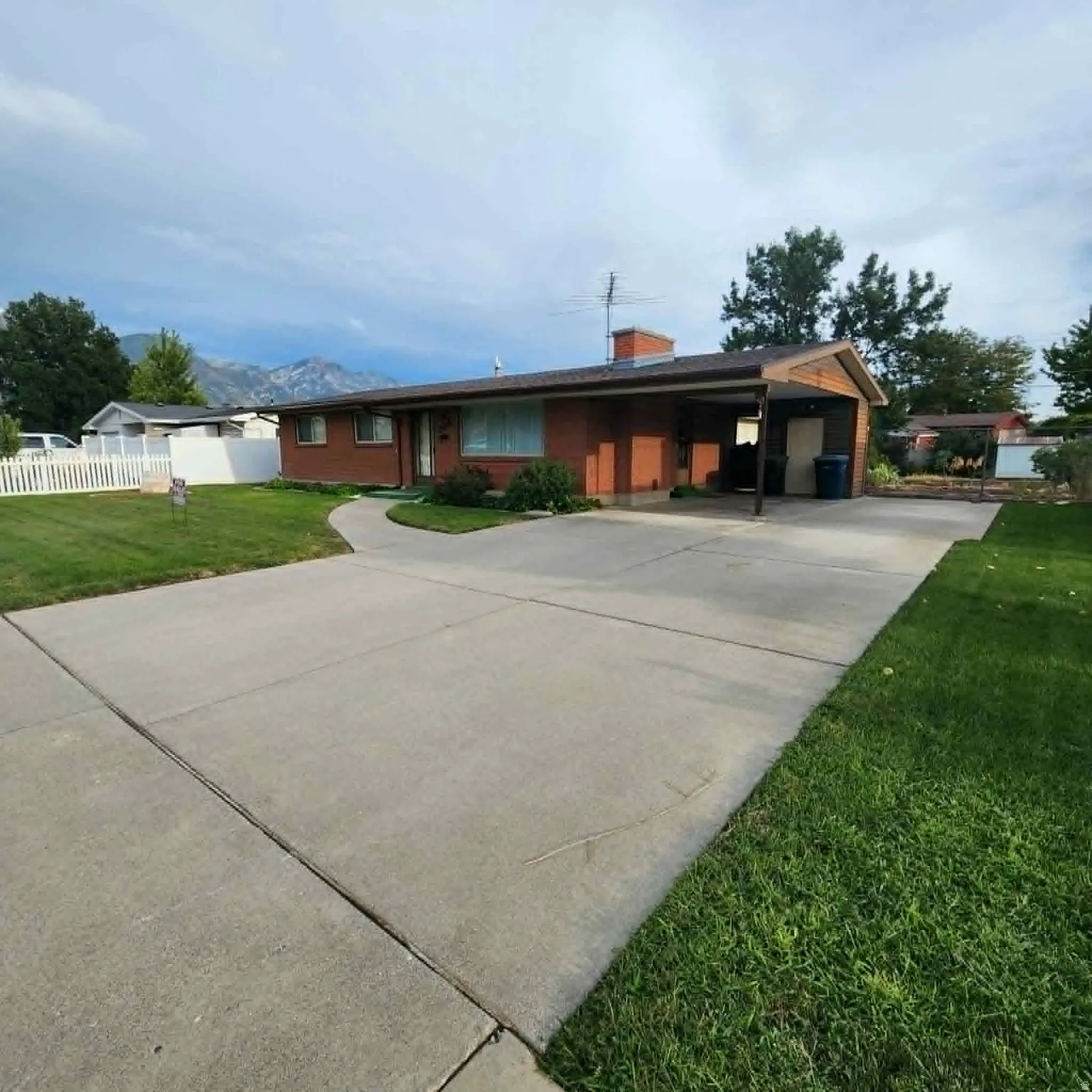 Brick exterior with a covered carport, concrete driveway, and front lawn