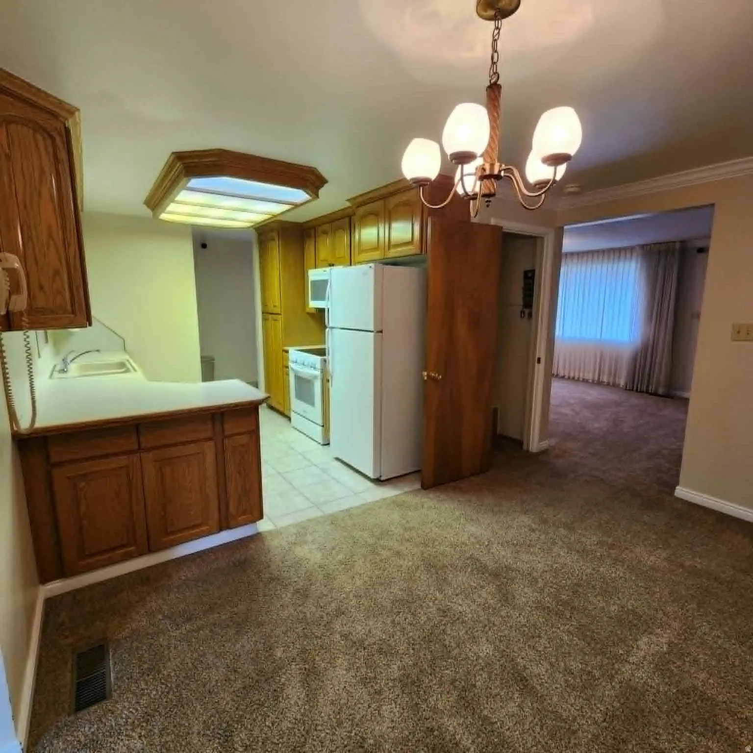 Kitchen featuring wood cabinetry, white appliances, and a fluorescent ceiling light