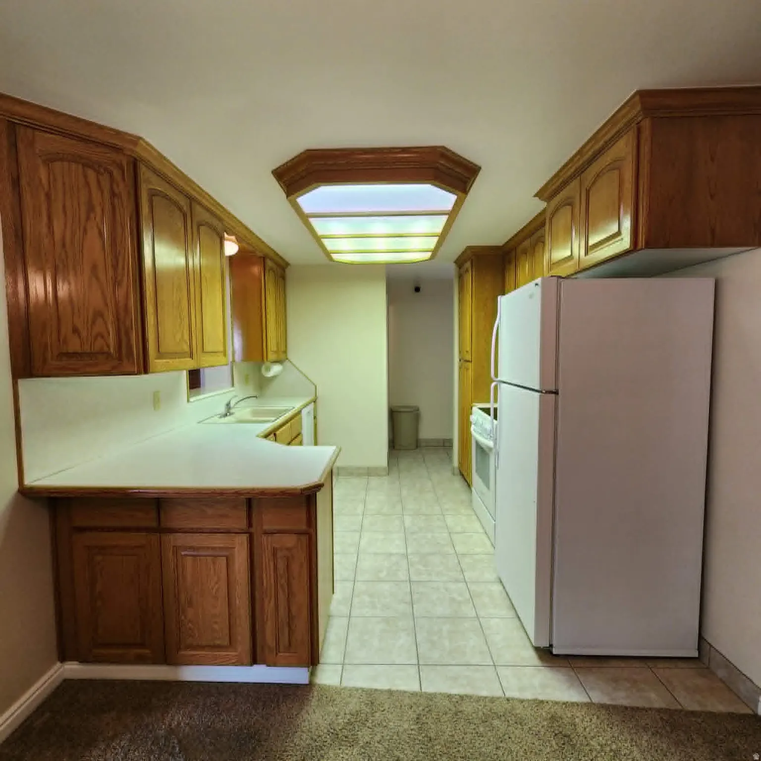 Kitchen featuring wood-finish cabinetry, white countertops, a drop-in sink, and tile flooring