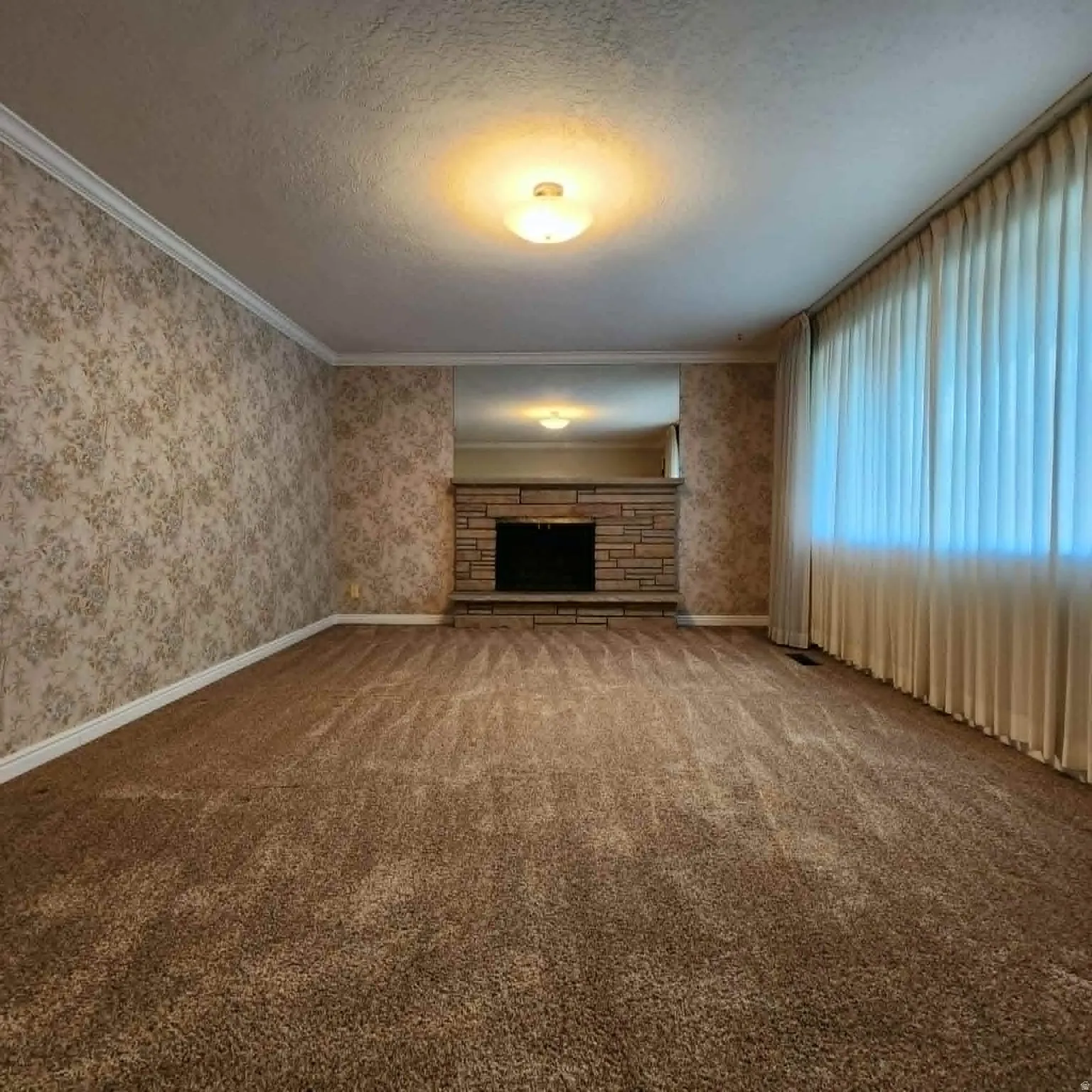 Stone fireplace with hearth, wall-to-wall carpeting, crown molding, and decorative wallpaper