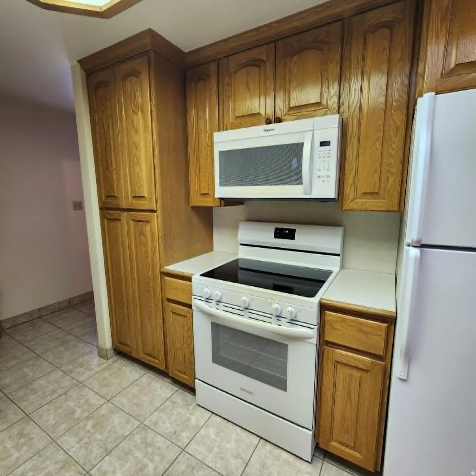 Wood cabinetry with crown molding, white countertop space, white over-the-range microwave, and white electric range