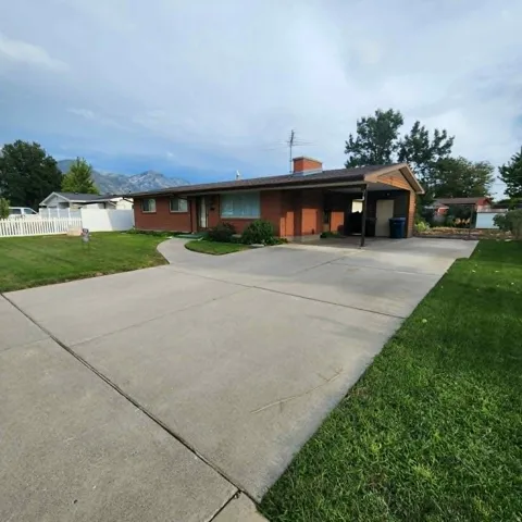 Brick exterior with a covered carport, concrete driveway, and front lawn