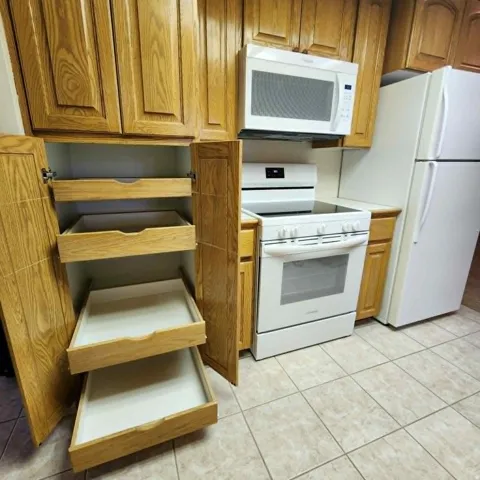 Kitchen featuring wood-finish cabinetry, tile flooring, white electric range, and a white microwave oven