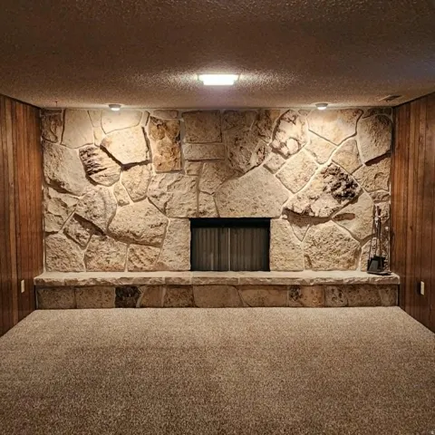 Stone fireplace with a hearth, integrated firebox, wall-mounted lighting, and carpeted flooring