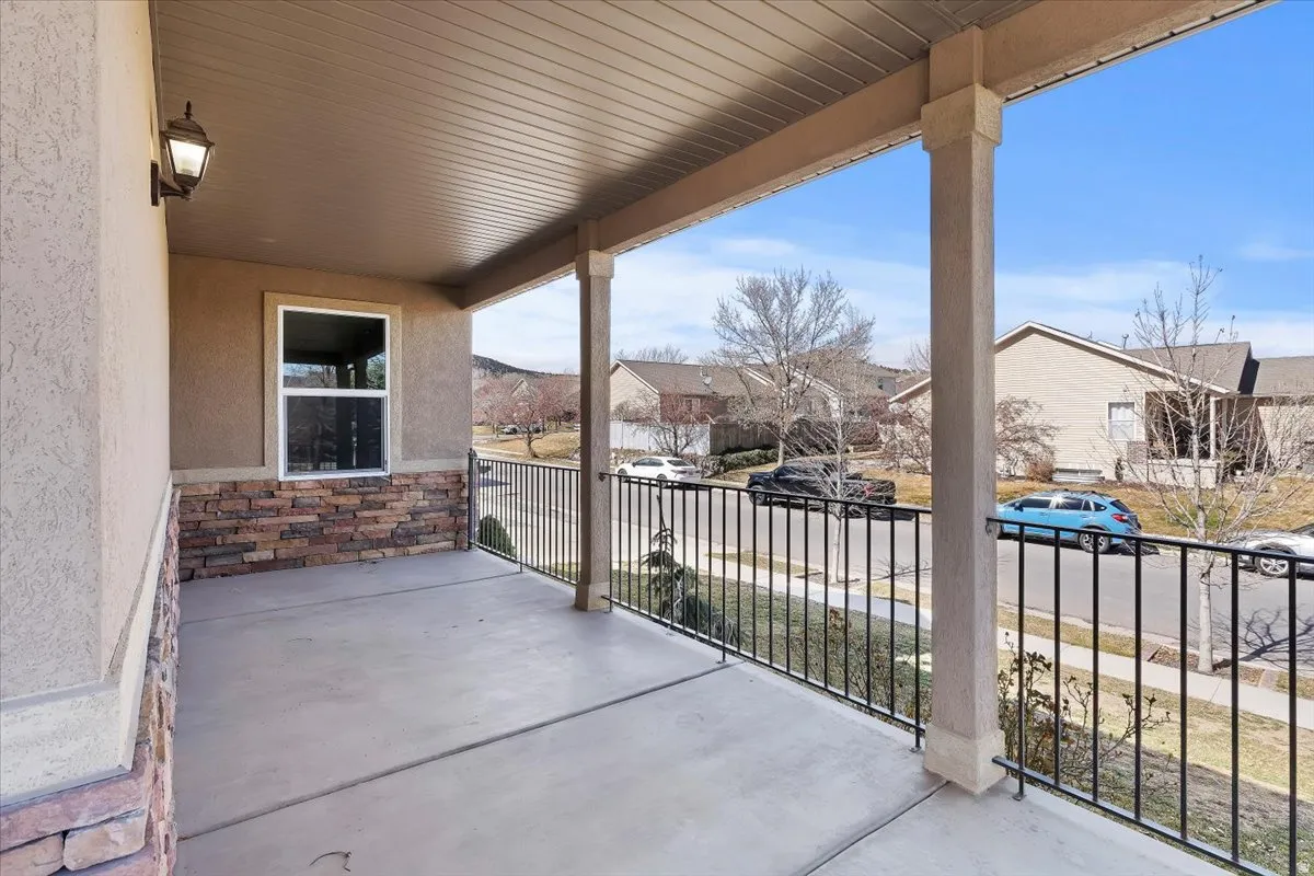 Covered porch with concrete flooring, stone veneer detailing, stucco exterior, and black metal railings