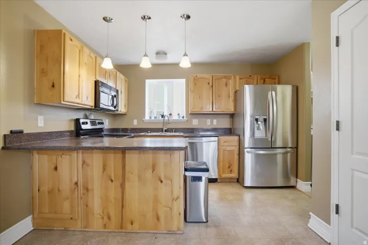 Kitchen featuring natural wood cabinetry, stainless steel appliances, speckled countertops, and an undermount sink
