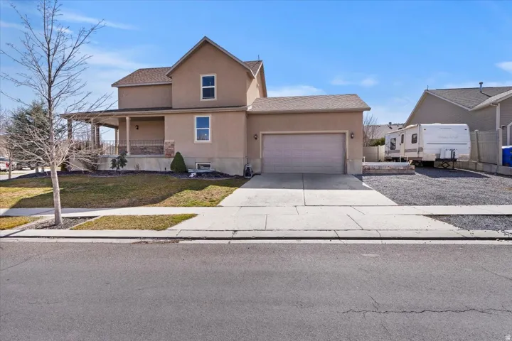 Two-story stucco exterior with an attached garage, covered front porch, and a gravel side parking area