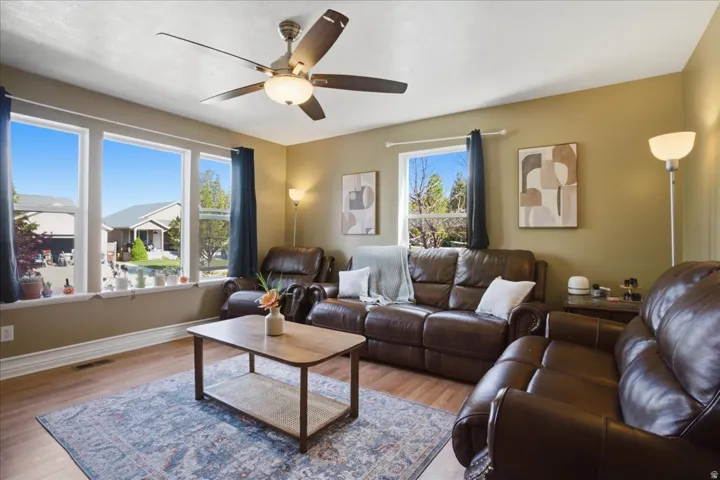 Wood-finish flooring, multiple large windows, and a ceiling fan with integrated lighting