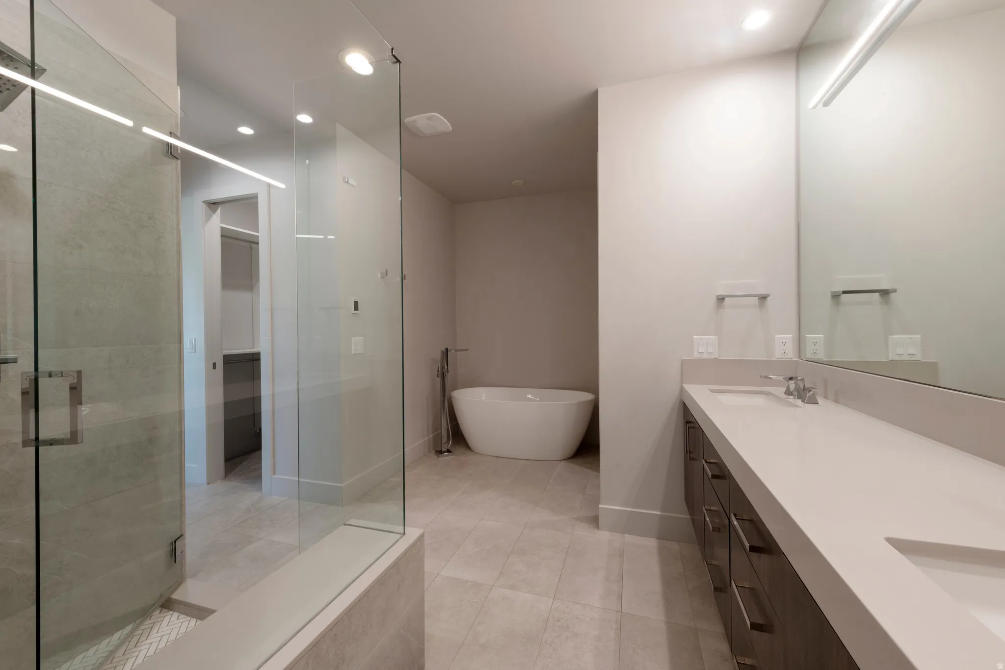 Spacious bathroom featuring a frameless glass shower, freestanding soaking tub, dual vanity with undermount sinks, and large format floor tiling