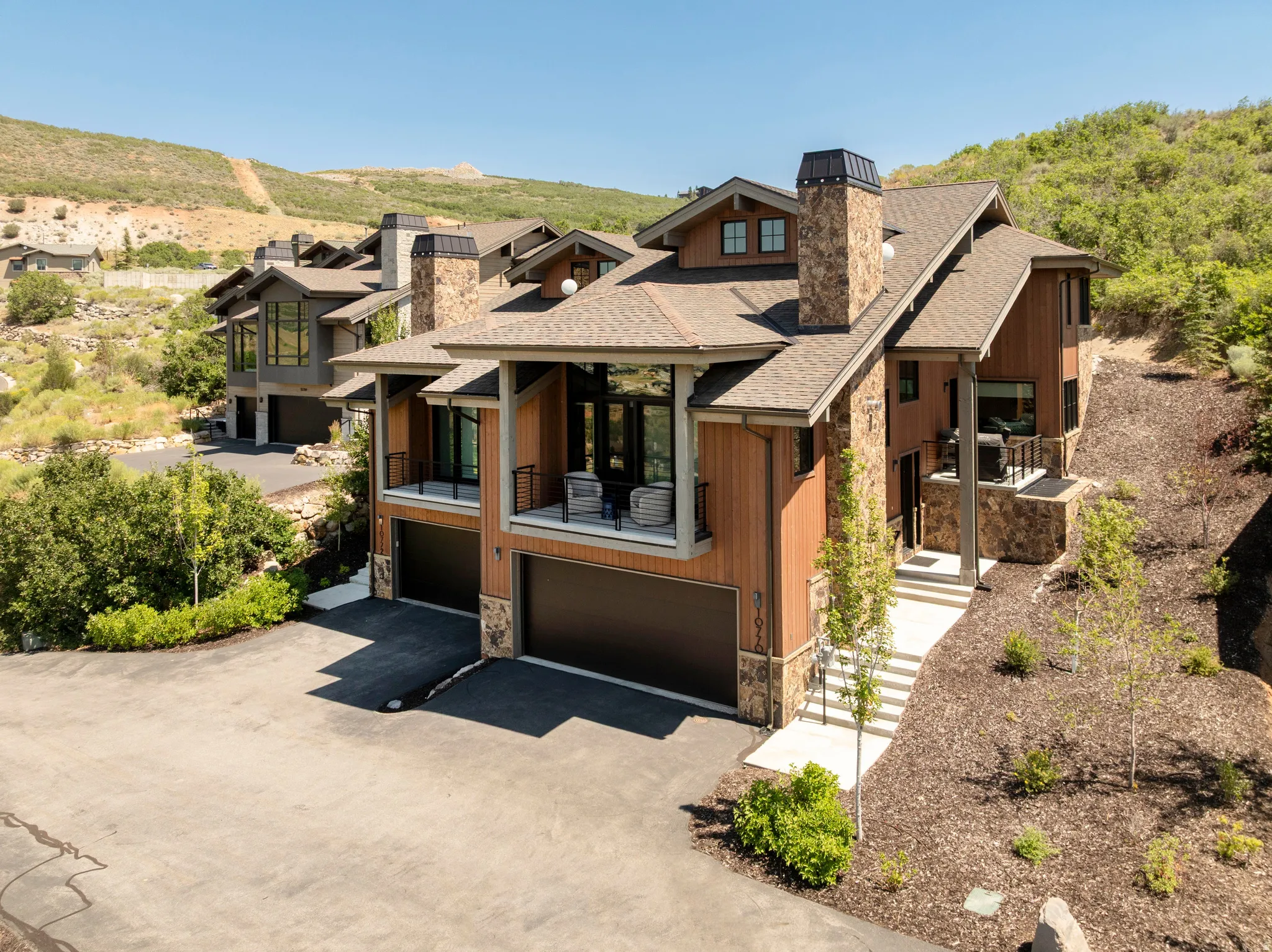 Stone and wood-sided exterior featuring multiple balconies, prominent stone chimneys, and a multi-level asphalt driveway