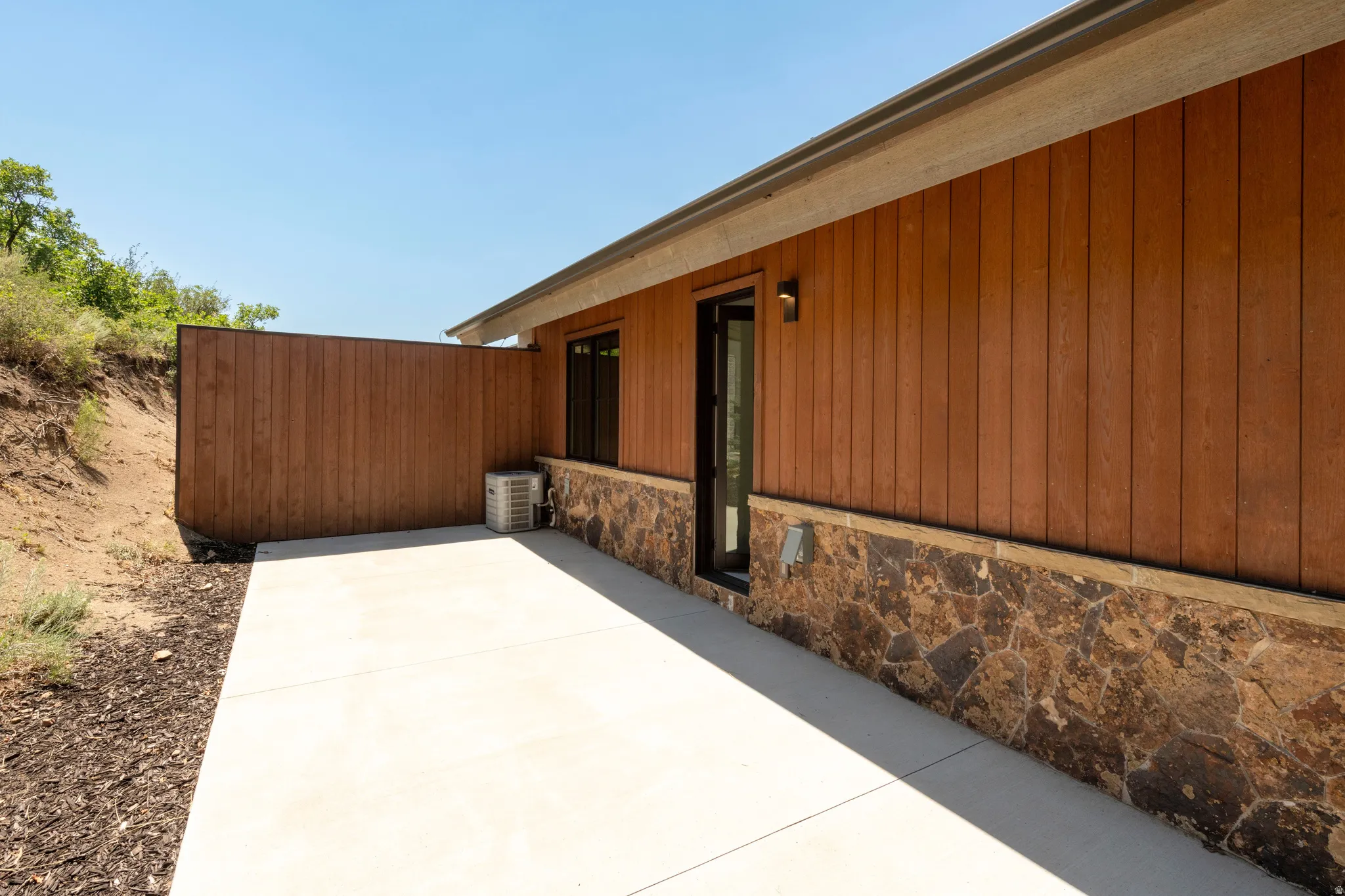 Spacious concrete patio with a privacy wall, featuring a wood-panel exterior and stone veneer detailing