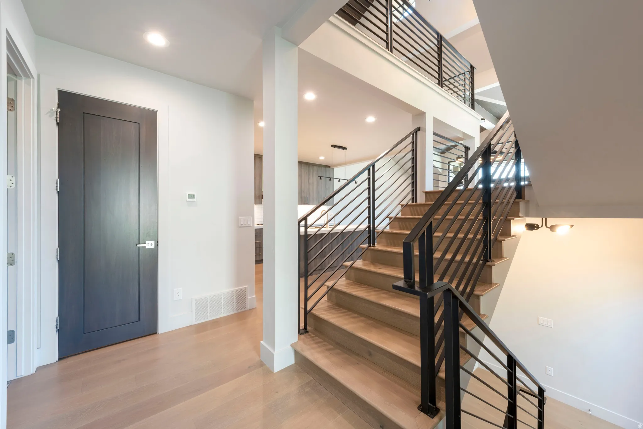 Light wood-finish flooring, dark wood-finish interior door, recessed lighting, wood-finish staircase with metal railings, and a two-tier chandelier