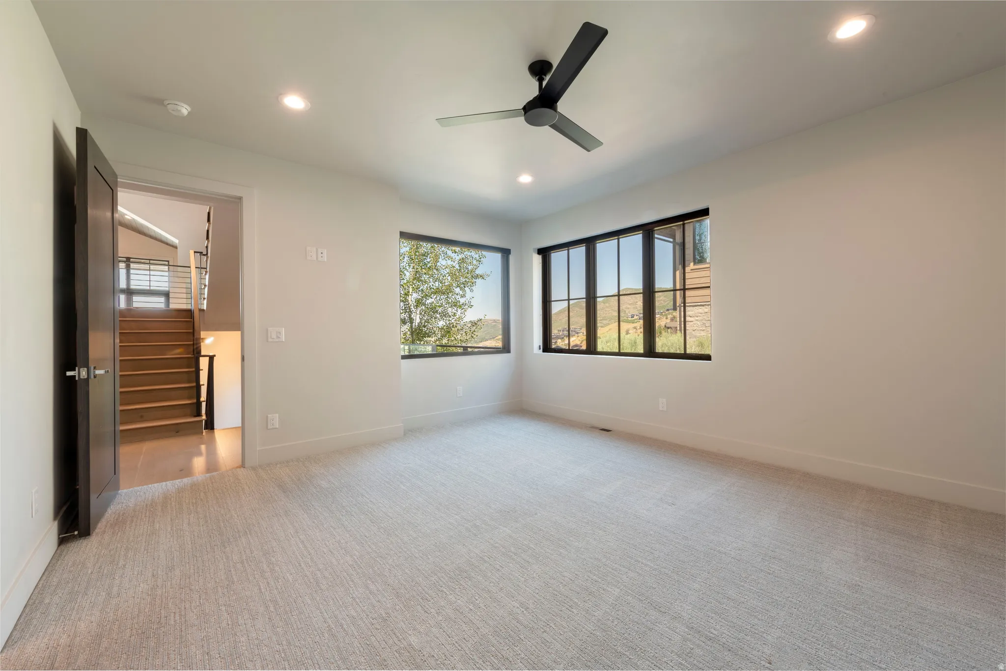 Recessed lighting, ceiling fan, dark-framed windows, light-toned carpeting, and wood stairs