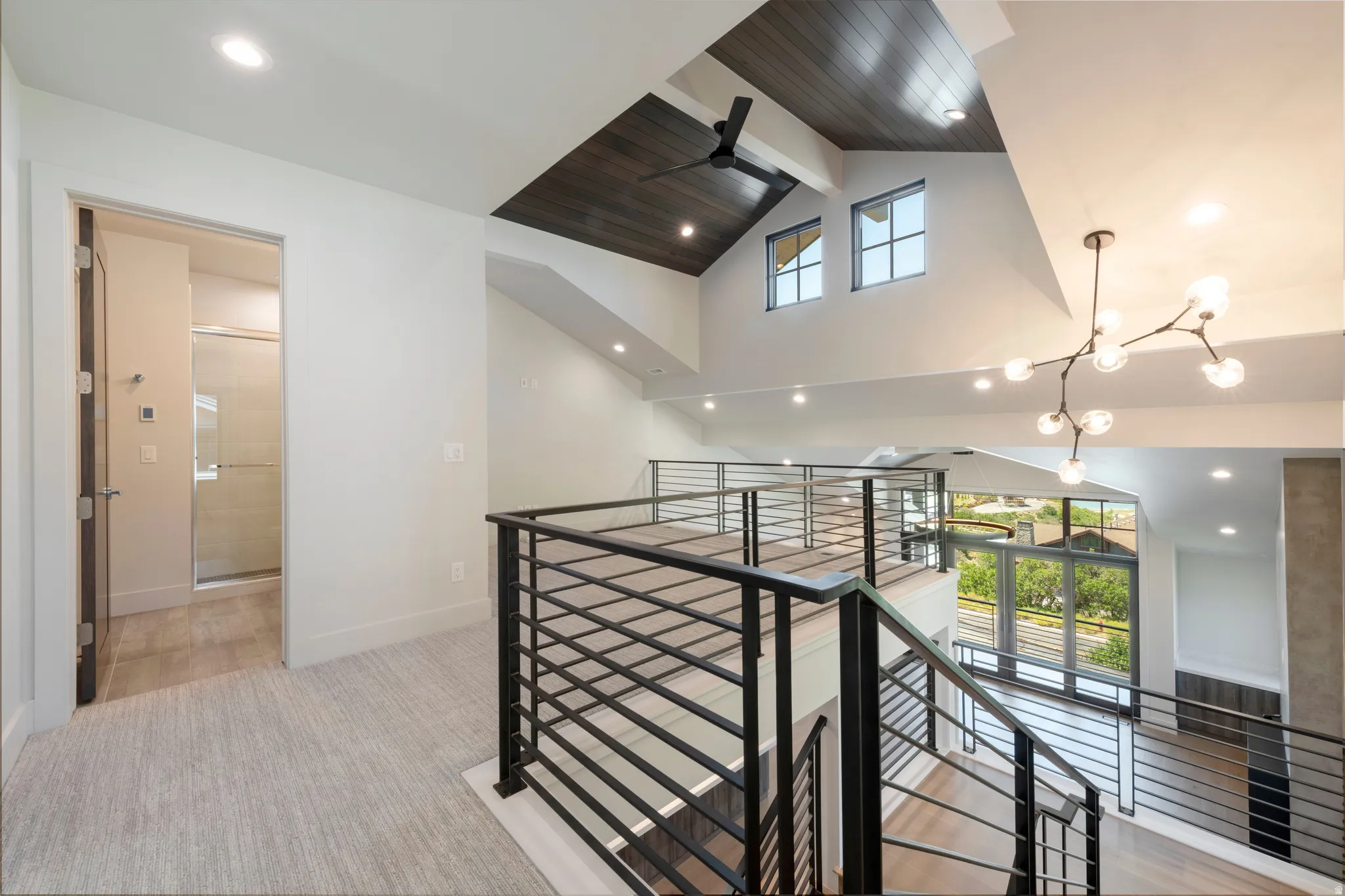 Open loft area with wood-finish vaulted ceiling, contemporary chandelier, and metal railing