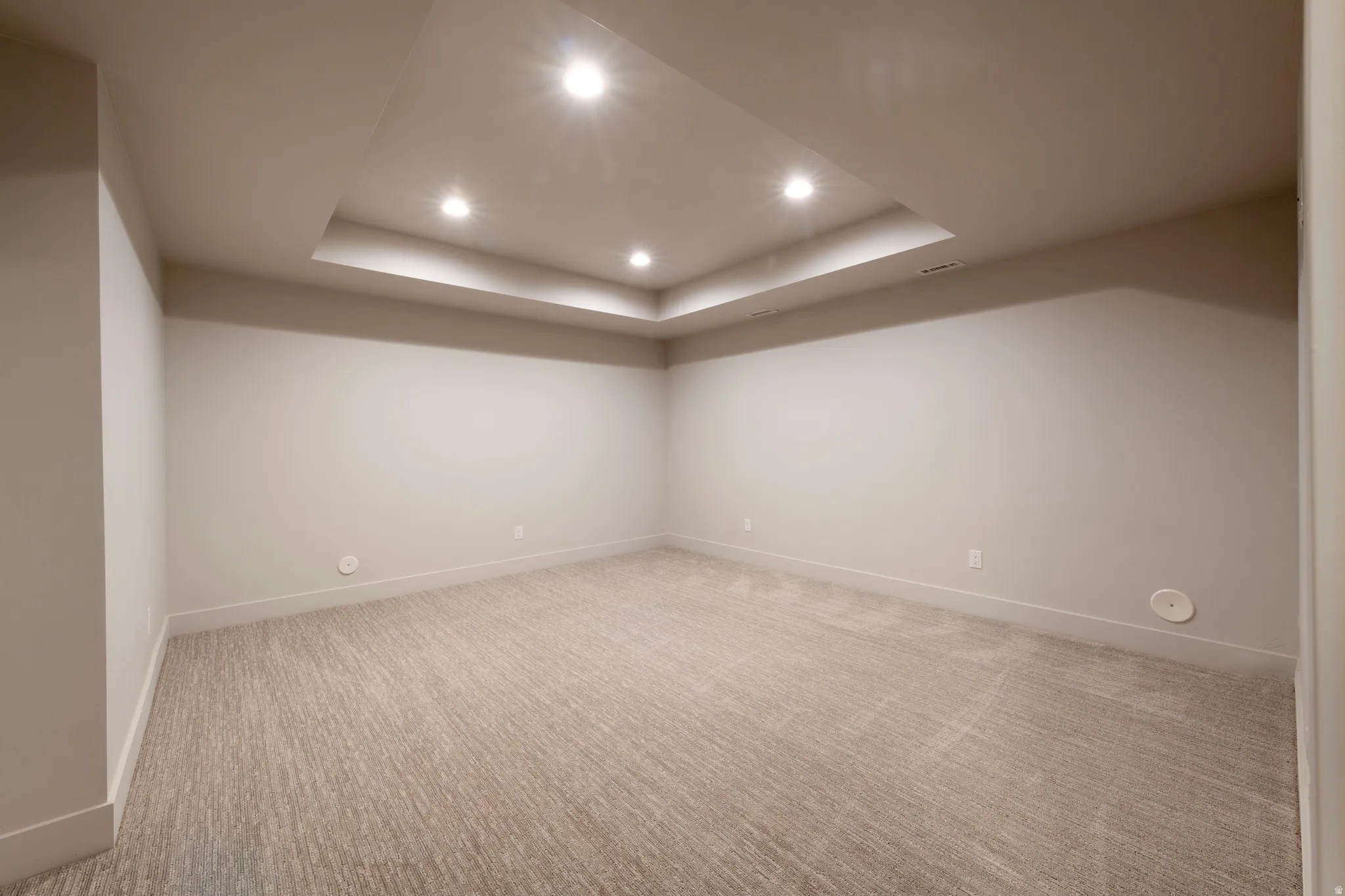 Recessed tray ceiling with integrated lighting, neutral wall finishes, wide baseboards, and textured carpeting