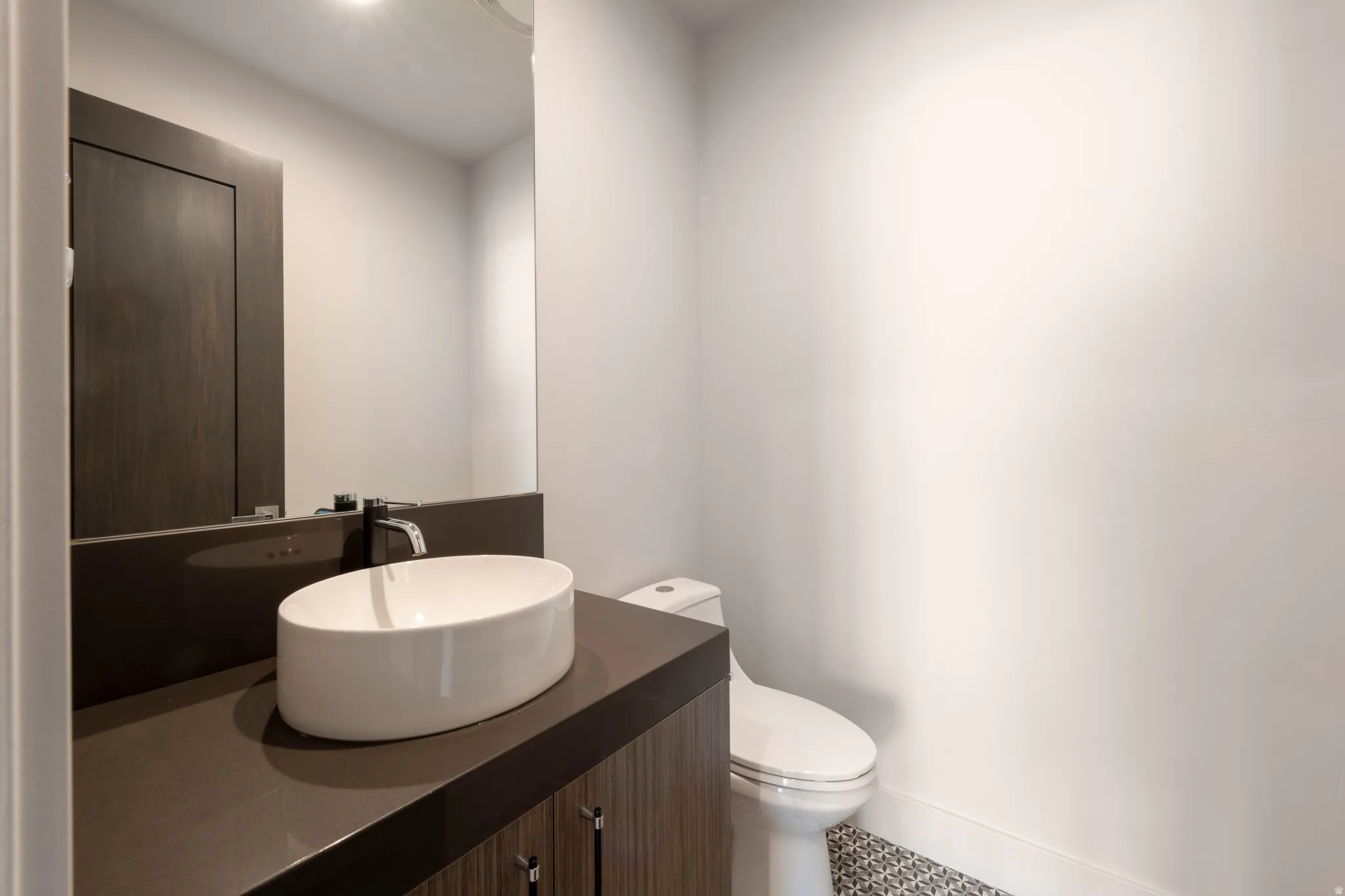 Contemporary vanity with a vessel sink, dark countertop, and integrated mirror
