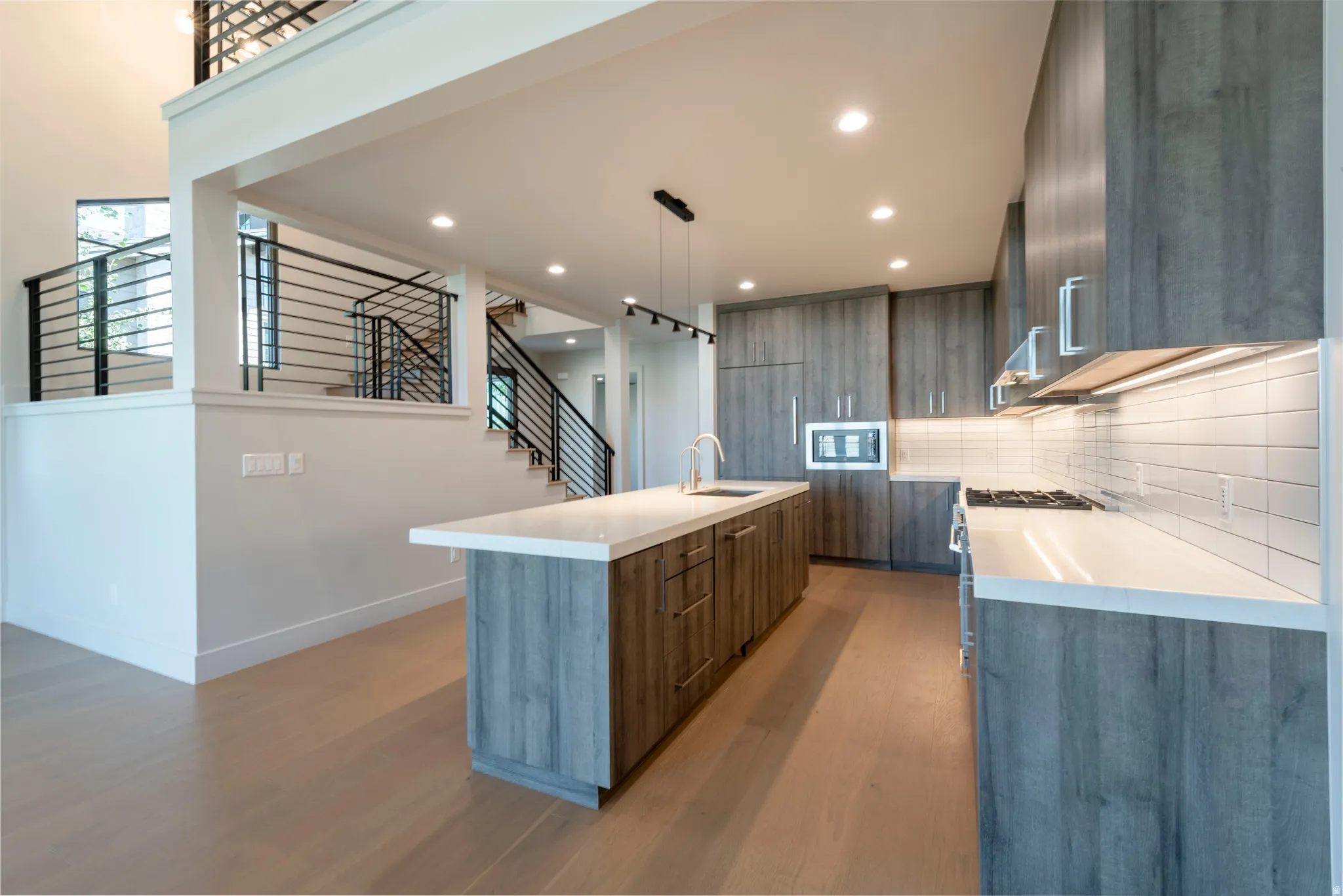 Contemporary kitchen featuring wood-finish cabinetry, white countertops, stainless steel appliances, and a tile backsplash