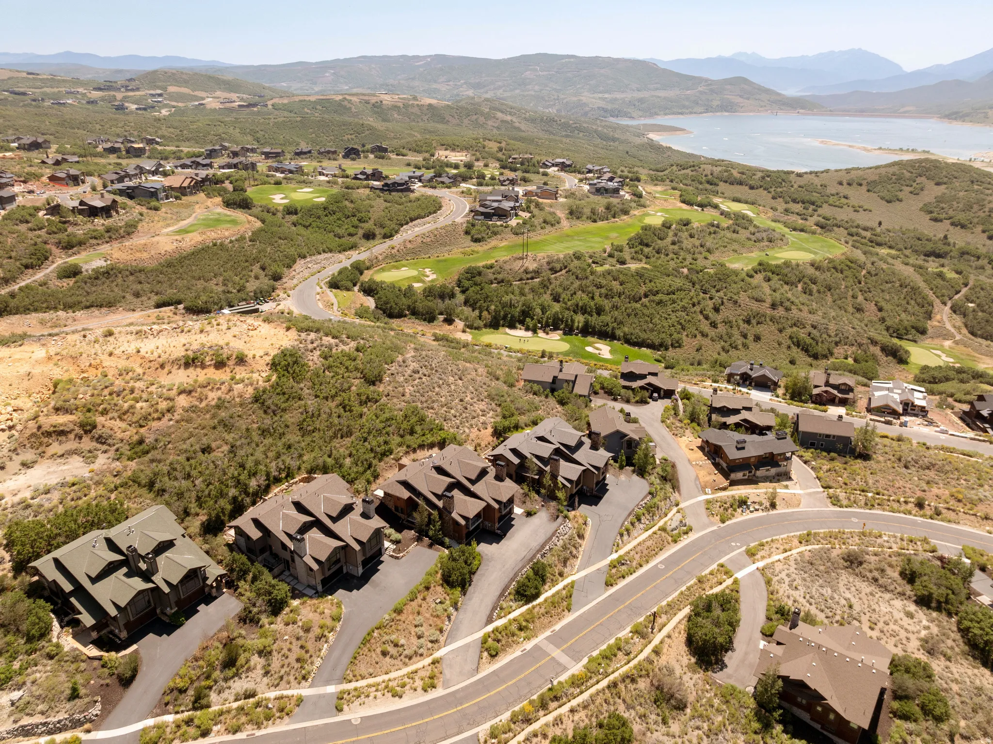 Expansive mountain landscape with scattered residential properties, a golf course, and a distant body of water