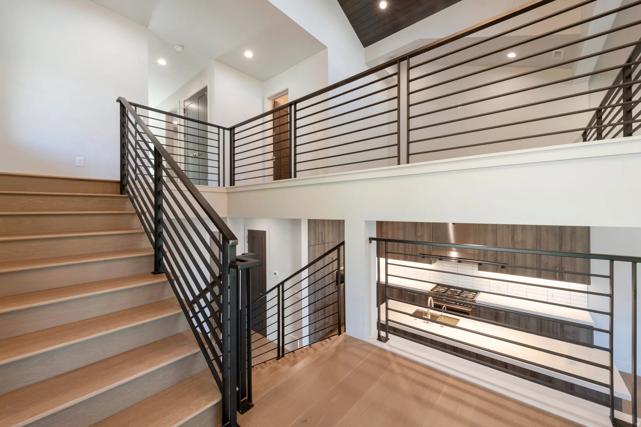 Open-concept layout with wood-finish flooring, black metal railings, recessed lighting, and a vaulted ceiling