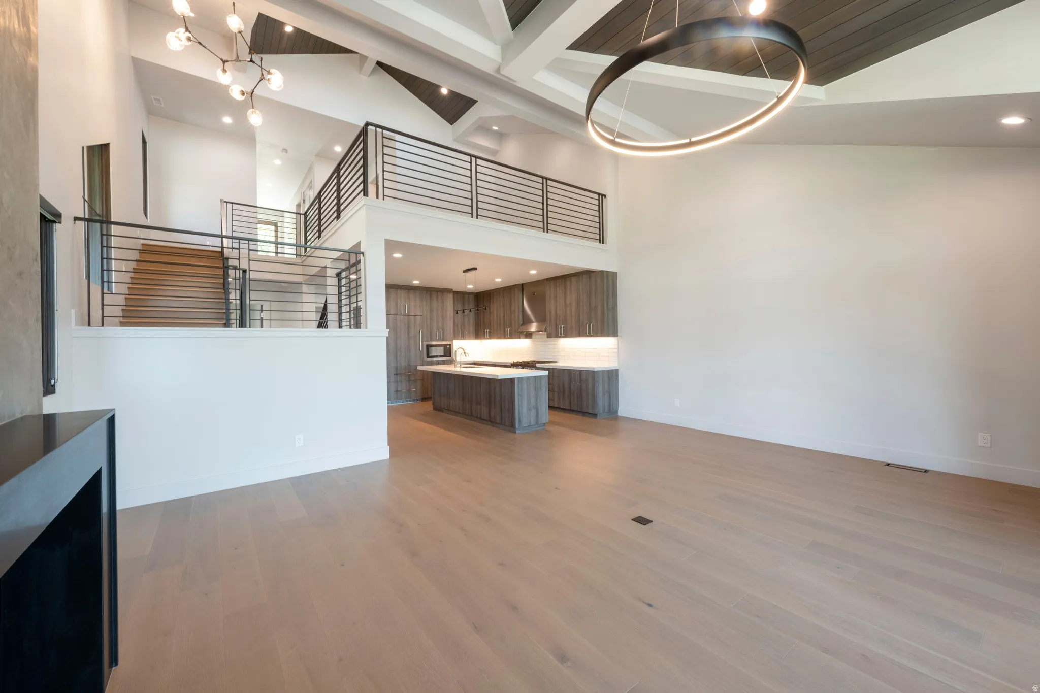 Cathedral ceilings with exposed beams, wood-finish flooring, a contemporary chandelier, a kitchen island with seating, and minimalist cabinetry