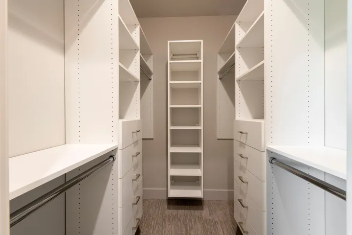 White built-in closet system featuring shelving, drawers with silver-tone hardware, and hanging rods