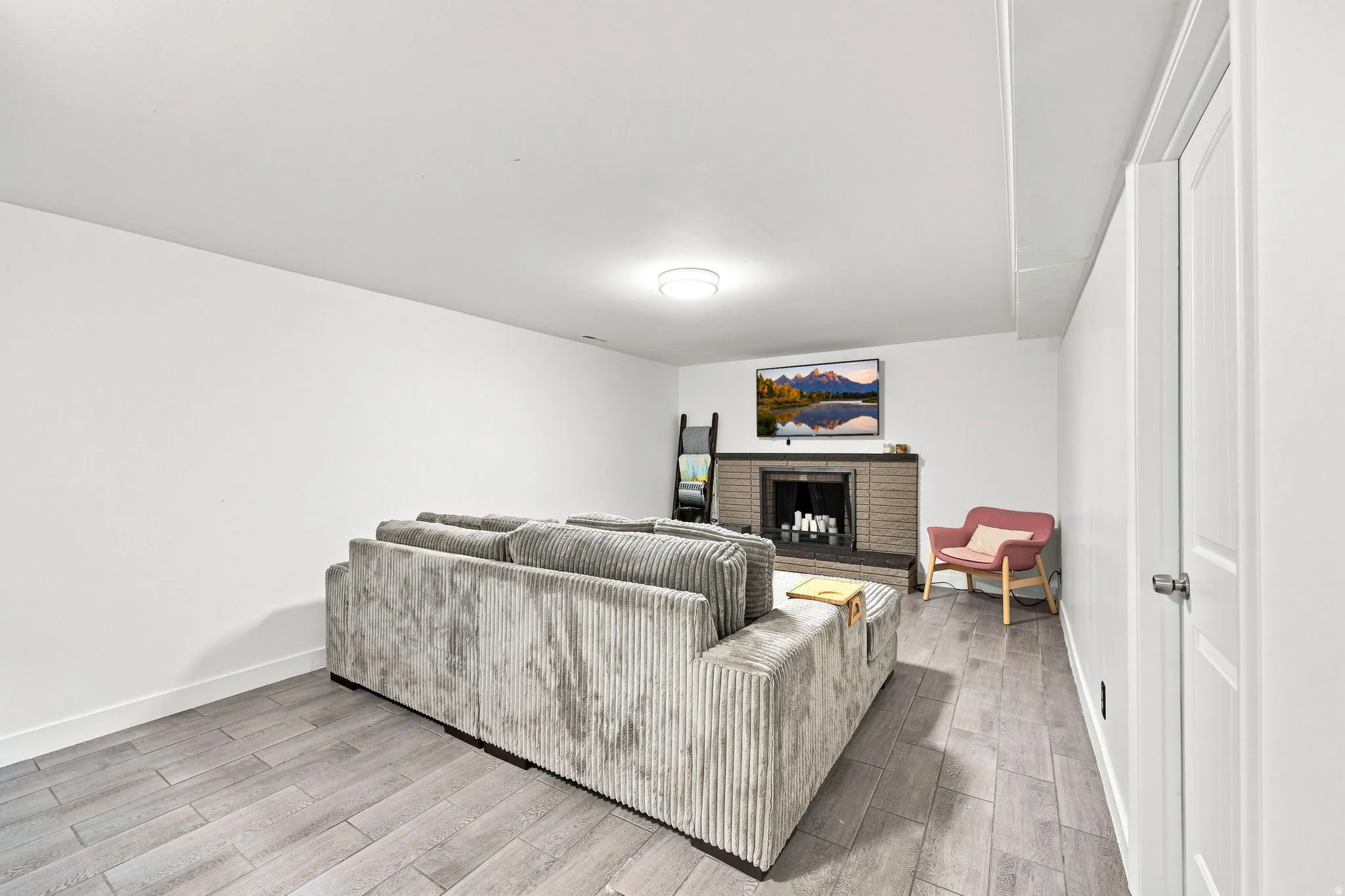 Wood-finish flooring, recessed lighting, brick-finish fireplace, white paneled door, and neutral wall tones