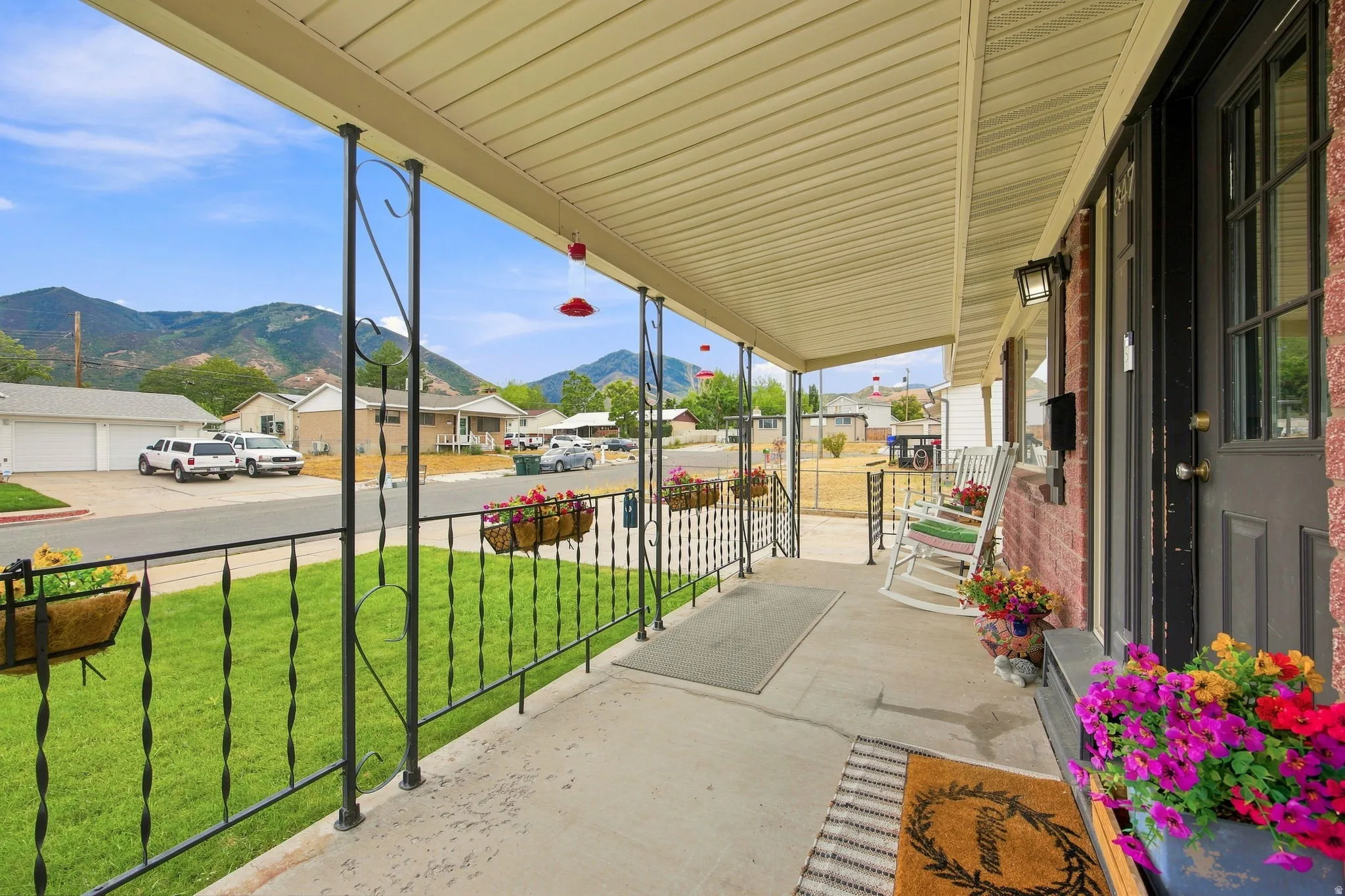 Covered front porch with concrete flooring, brick exterior, and decorative wrought iron railing