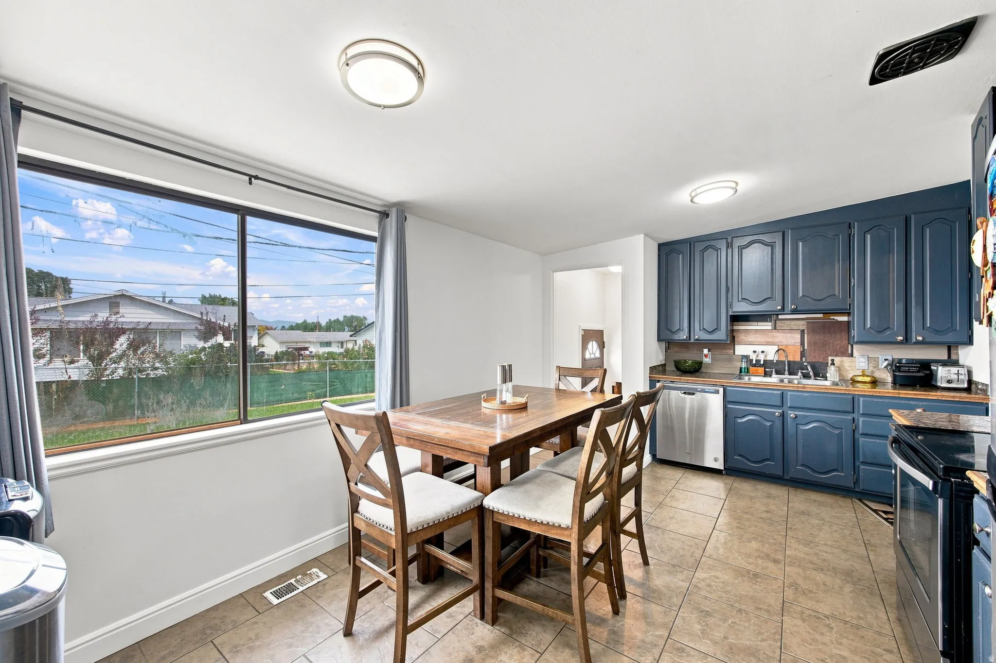 Expansive window, blue cabinetry, stainless steel dishwasher, tile flooring, and flush mount lighting