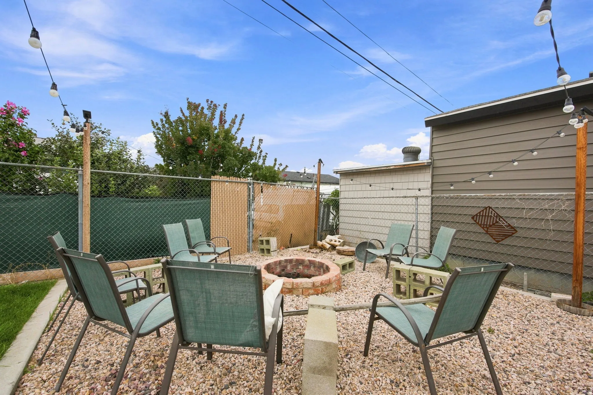Gravel patio with a brick fire pit, chain link fencing, and string lighting