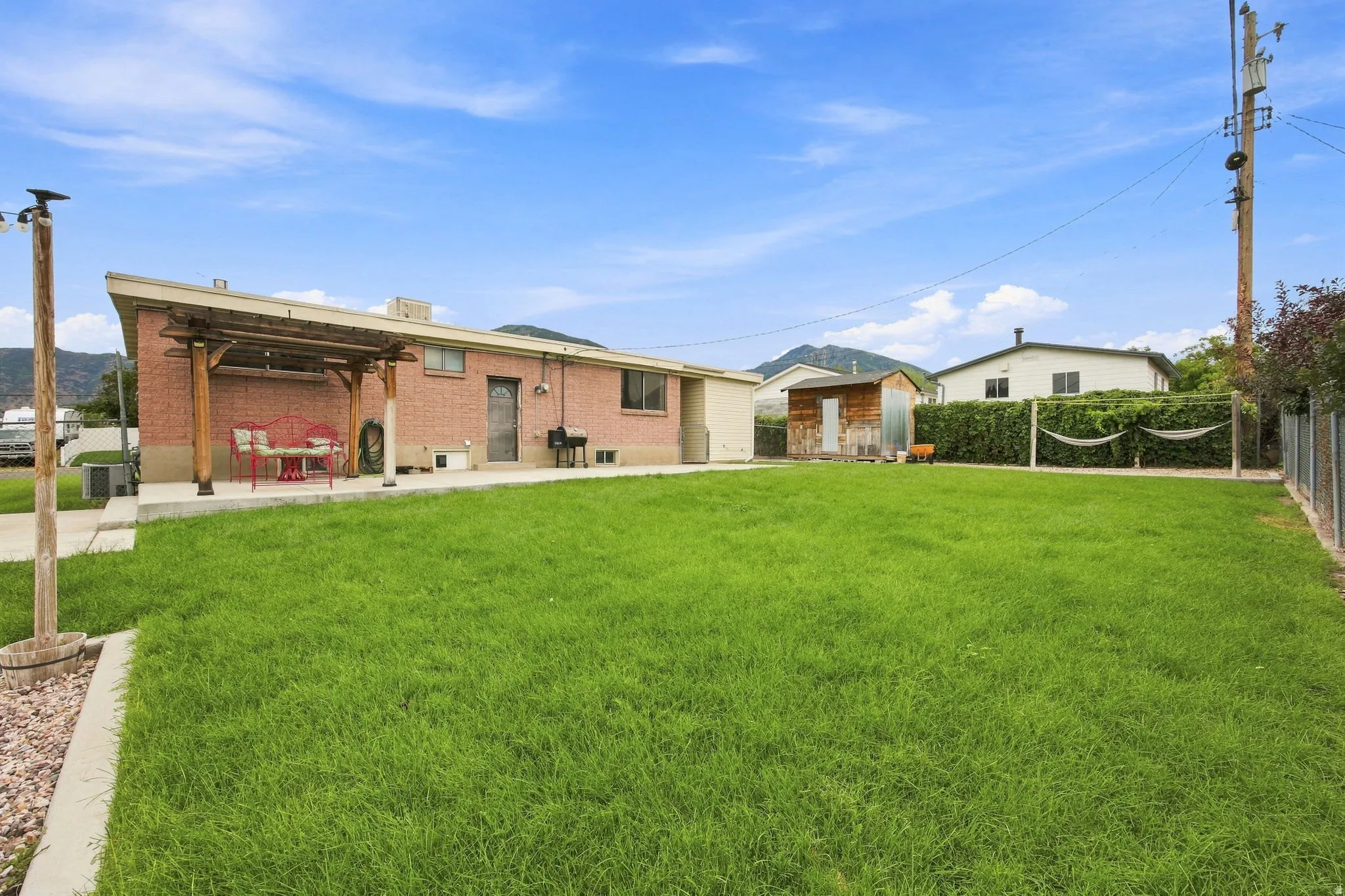 Expansive backyard featuring a manicured lawn, brick exterior, and a covered patio area