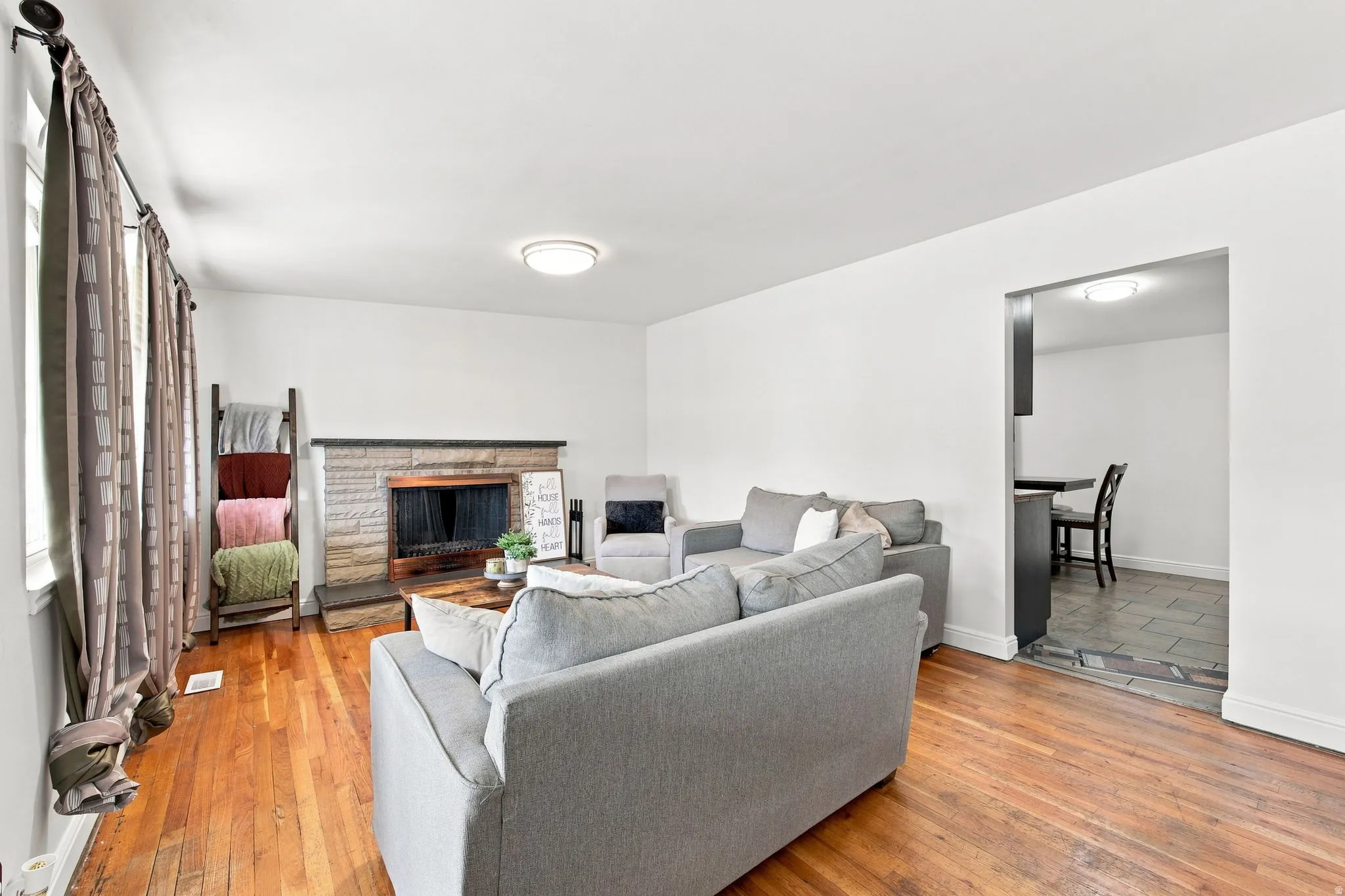 Wood-finish flooring, white walls, and a stone-faced fireplace with a dark mantel