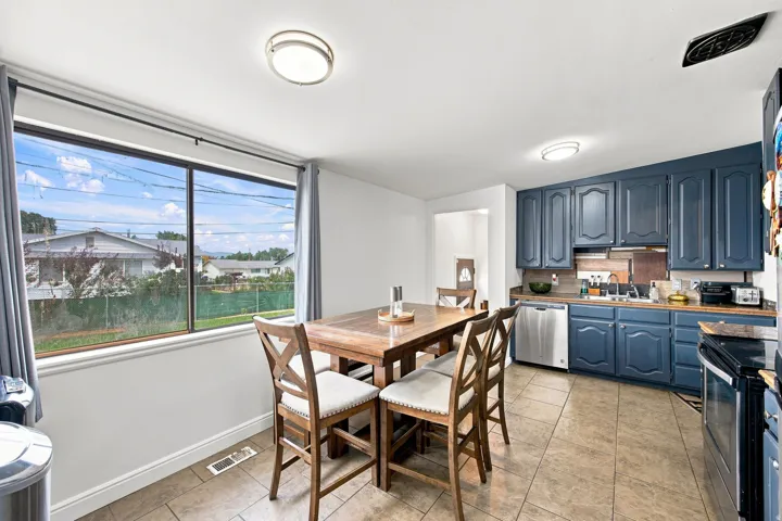 Expansive window, blue cabinetry, stainless steel dishwasher, tile flooring, and flush mount lighting
