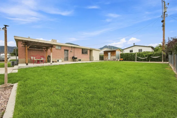Expansive backyard featuring a manicured lawn, brick exterior, and a covered patio area