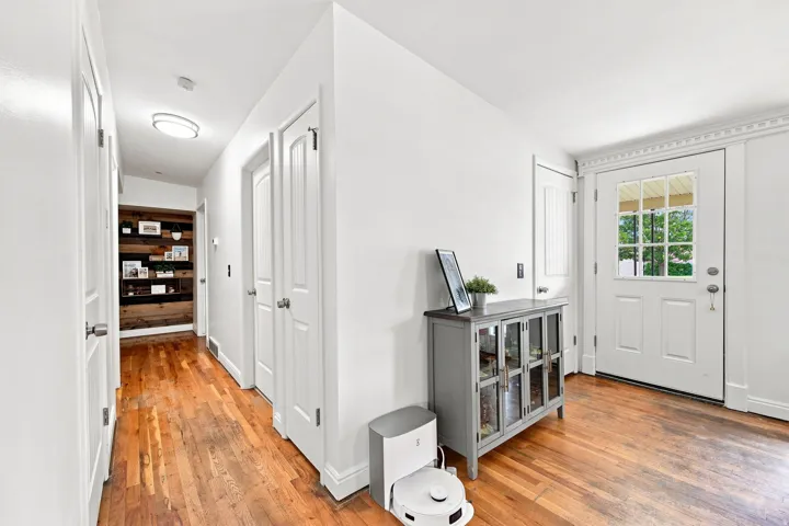 Hardwood flooring throughout, white interior doors, built-in shelving with wood plank detailing, and a front entry door with transom window