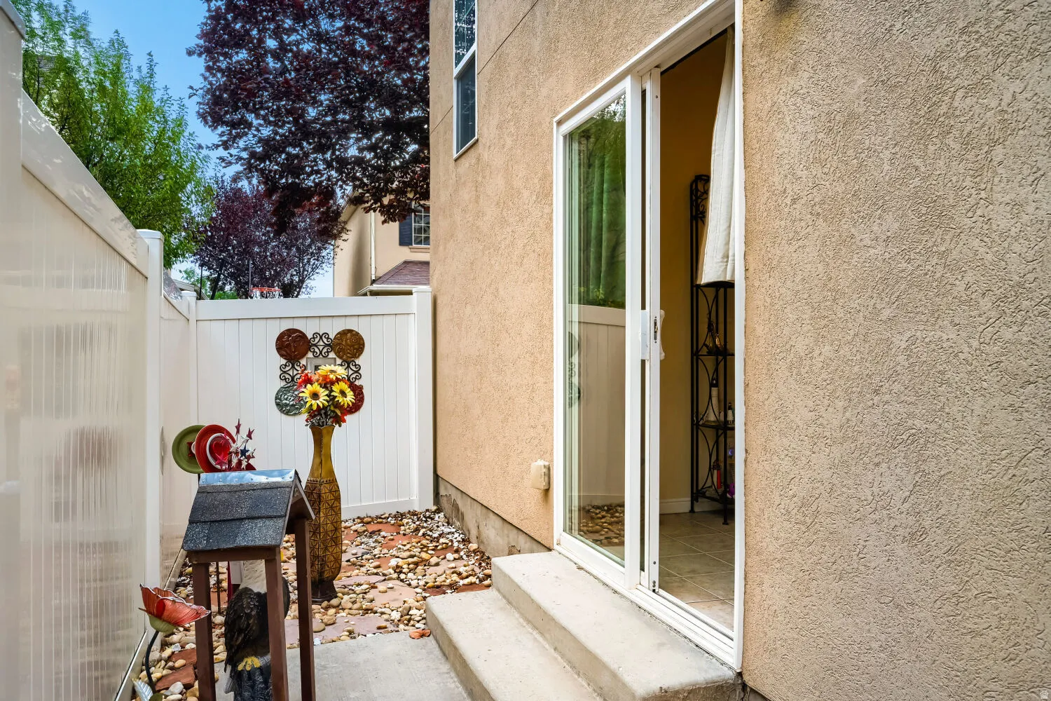 Private side yard featuring a white vinyl fence, decorative river rock, concrete steps, and a sliding glass door