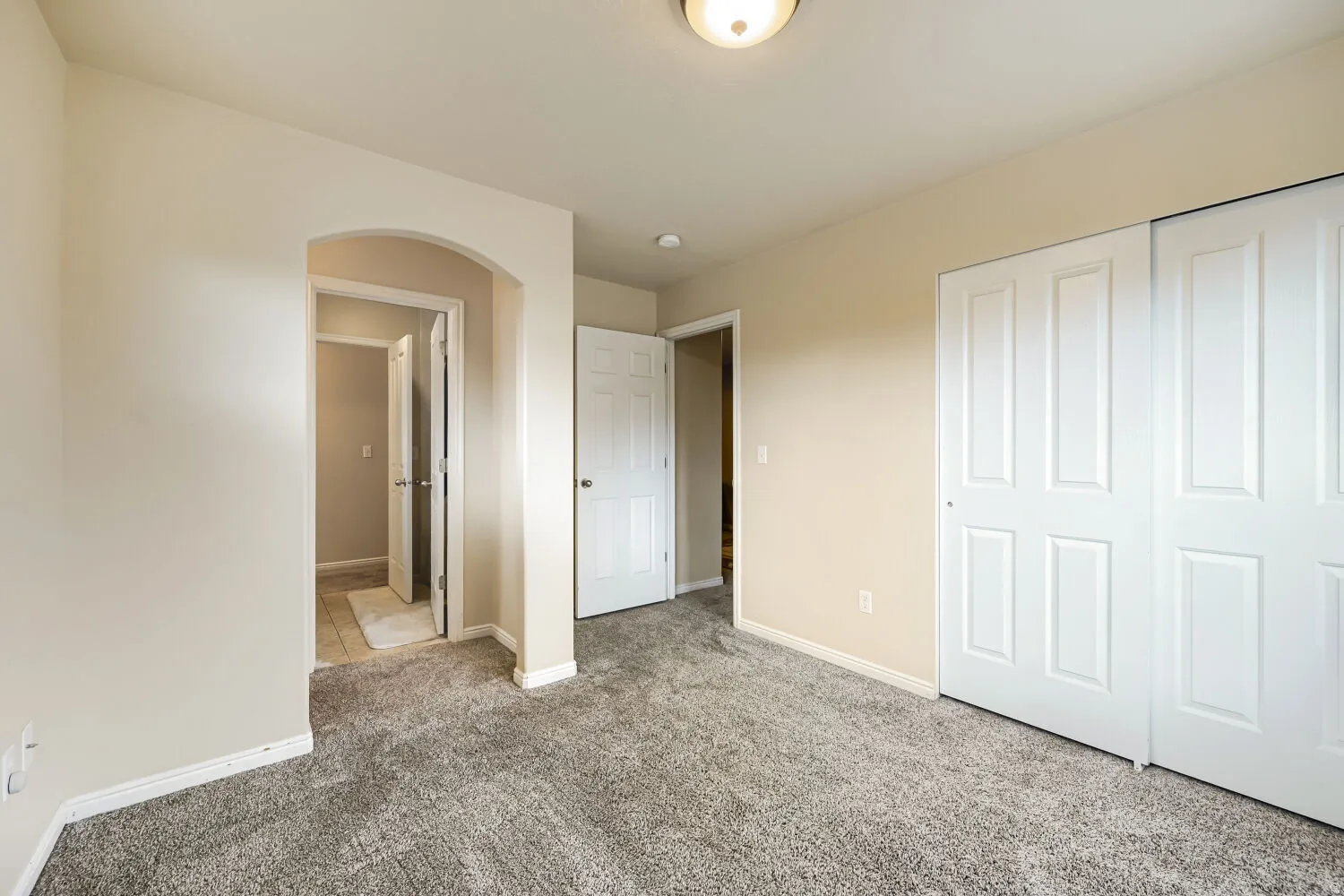 Archway entry to a tiled hallway, carpeted flooring, and white paneled bi-fold closet doors