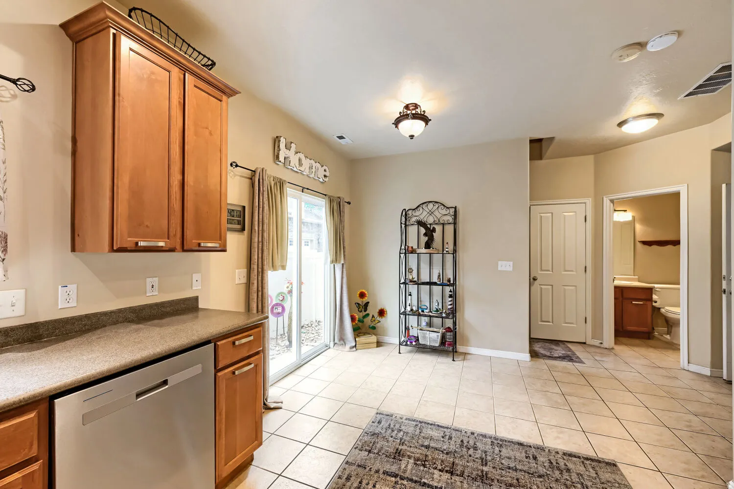 Tile flooring, wood-finish cabinetry, stainless steel dishwasher, sliding glass door, and a built-in vanity with a sink