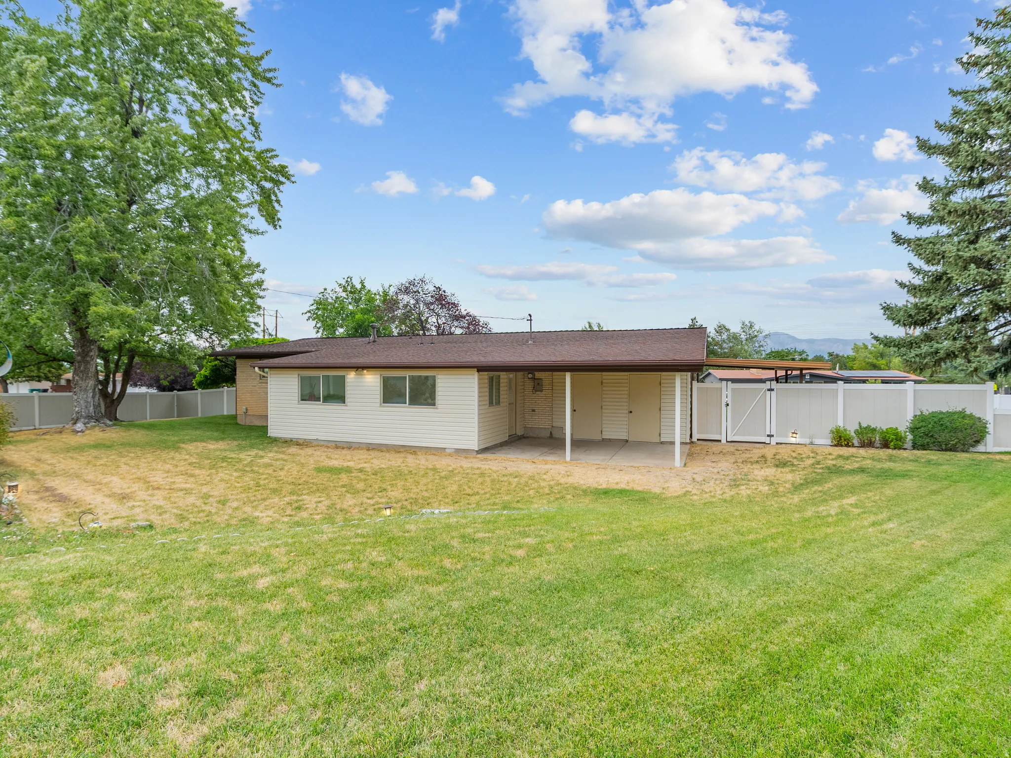 Expansive lawn with a covered patio, white fencing, and a mature shade tree
