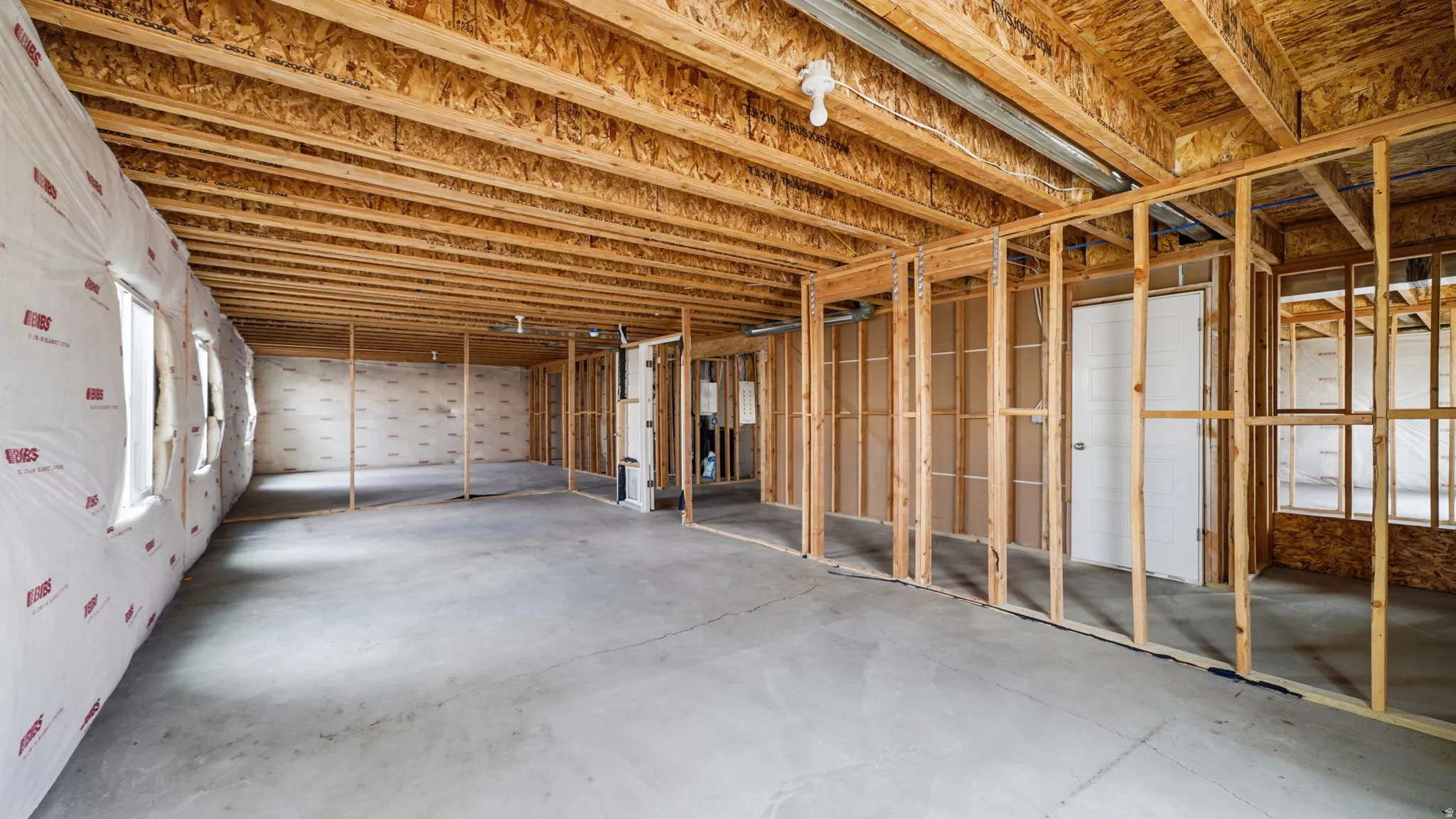 Unfinished basement with concrete flooring, exposed wood framing, multiple window openings, and an exposed wood joist ceiling